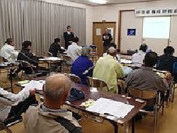 盛岡市・加賀野公民館での研修会・講義の様子(挨拶する事務局長と講師が写っています。参加者の後ろ姿が15人ほど写っています）